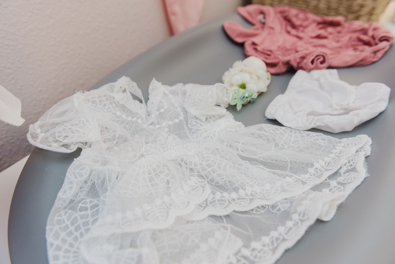 Lace details of pink and white baby clothing laid out on a gray surface.