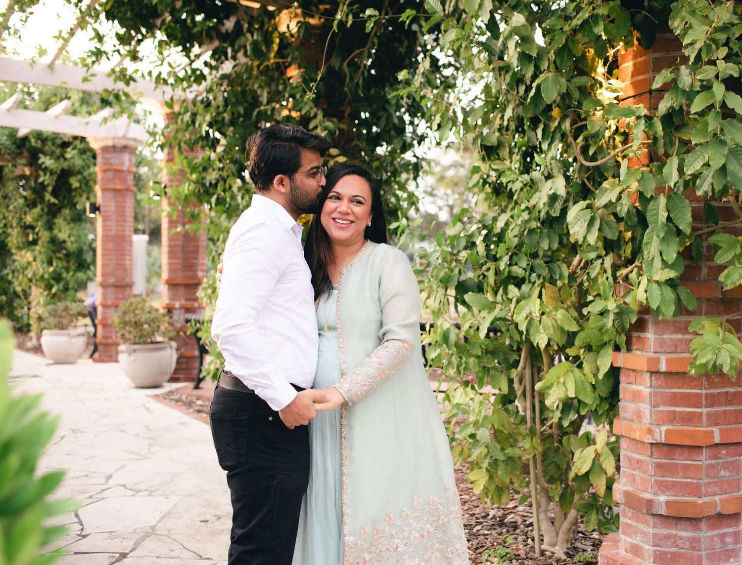 Couple sharing a romantic moment in a lush garden walkway with green foliage.