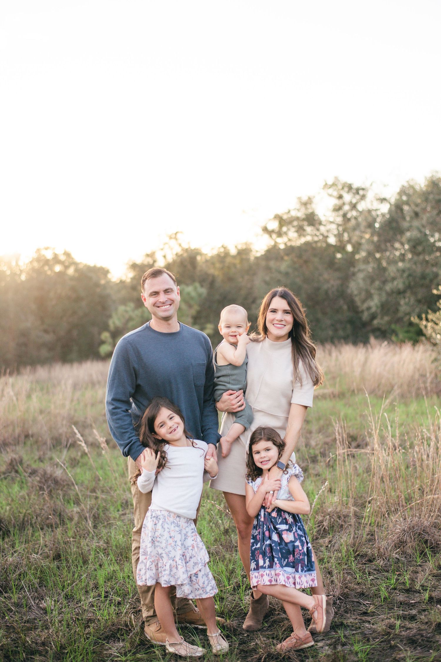 A group stands together in a sunlit field with tall grass at golden hour creating a warm family portrait atmosphere.