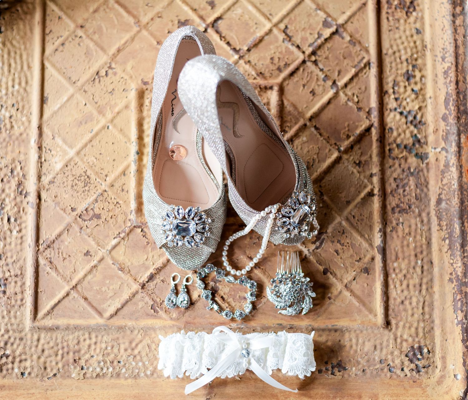 Elegant white bridal shoes and jewelry accessories arranged on a textured tile surface.