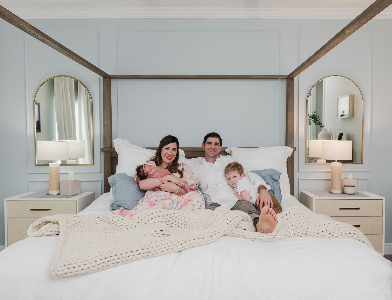 Family lounges together on white bed with matching decor in coordinated outfits.