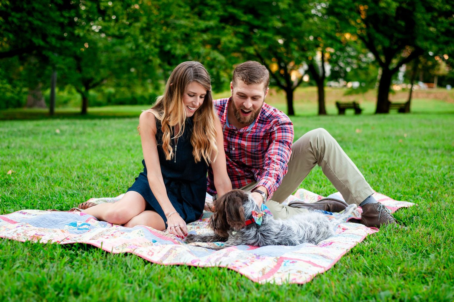 Couple relaxes on patterned blanket in park with their pet dog.