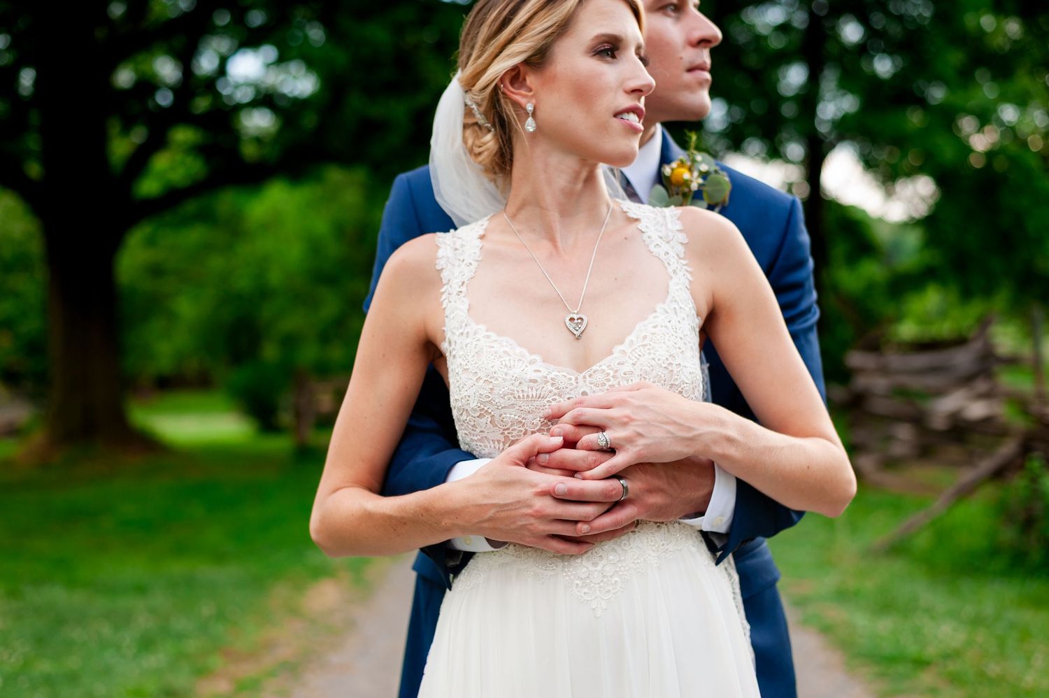 A wedding couple poses in a lush green garden setting with rustic barn backdrop.