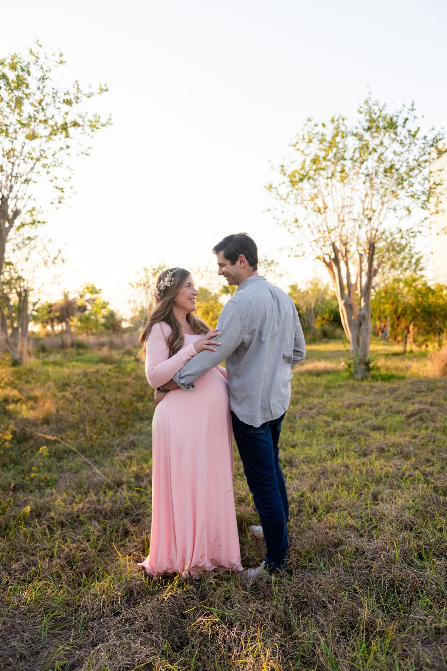 Two people share an intimate moment in a sunlit field during golden hour, wearing pink and blue outfits.