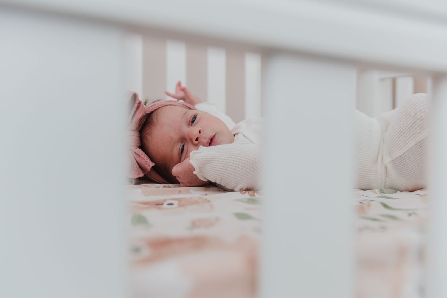 White crib bars frame a peaceful nursery scene with floral bedding.