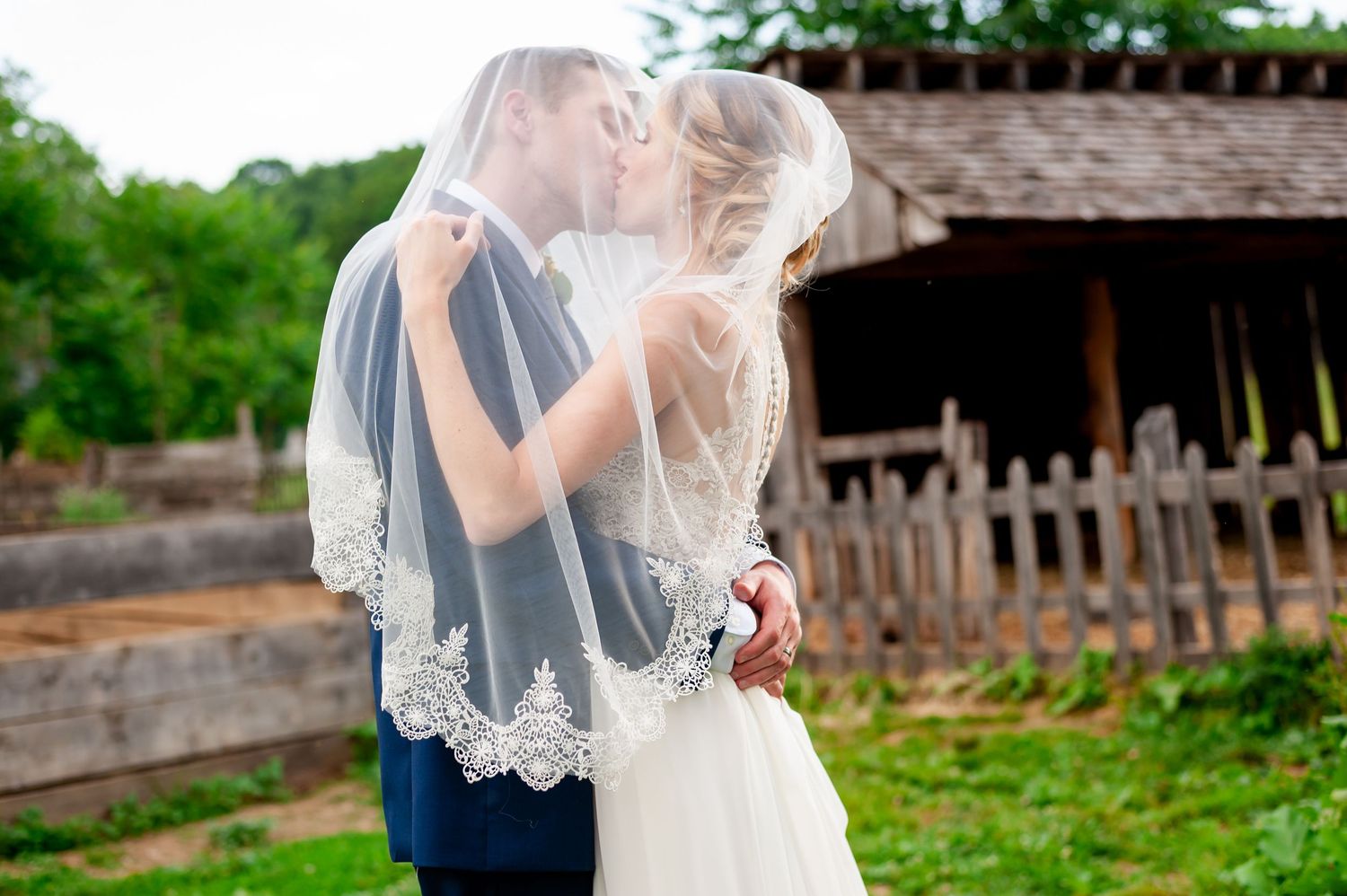 Wedding couple shares tender moment beneath ornate lace veil.