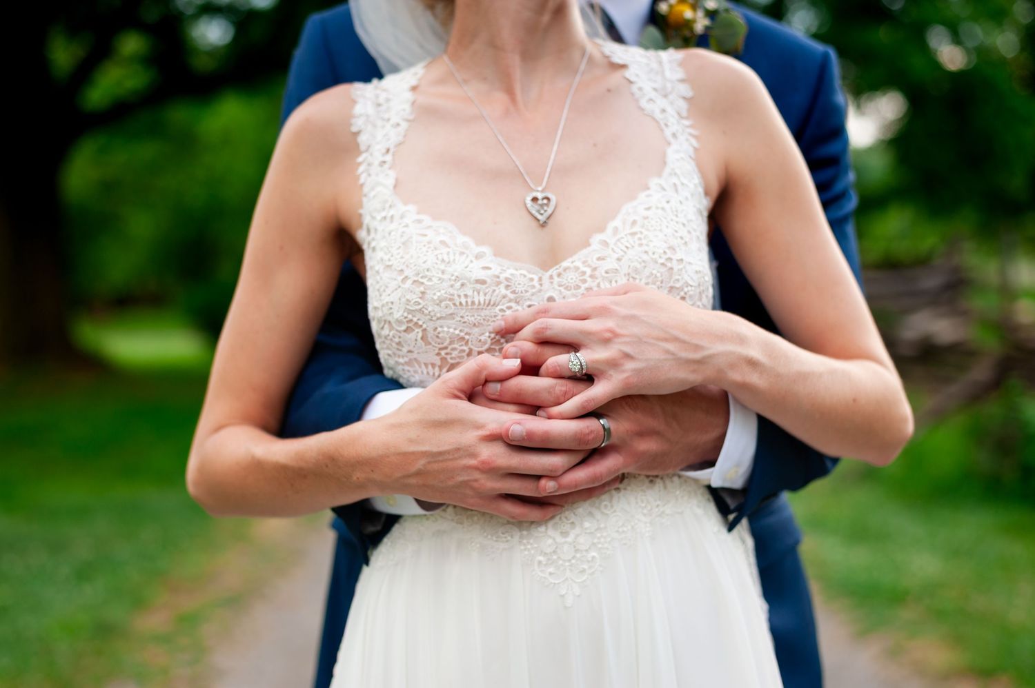 Close-up details of bride's lace dress and jewelry during outdoor wedding photography session.