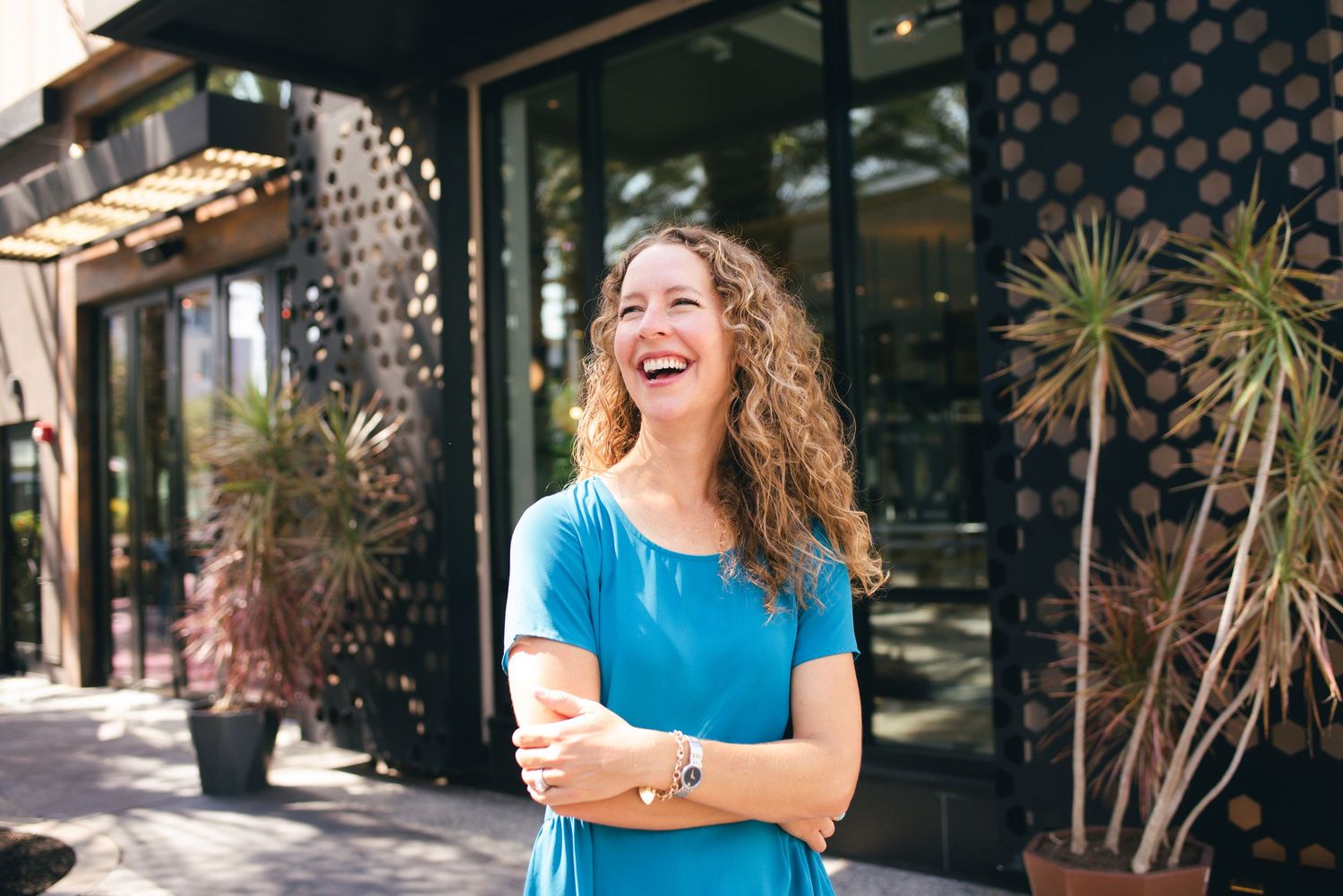 A cheerful portrait against modern architecture with decorative palm plants.