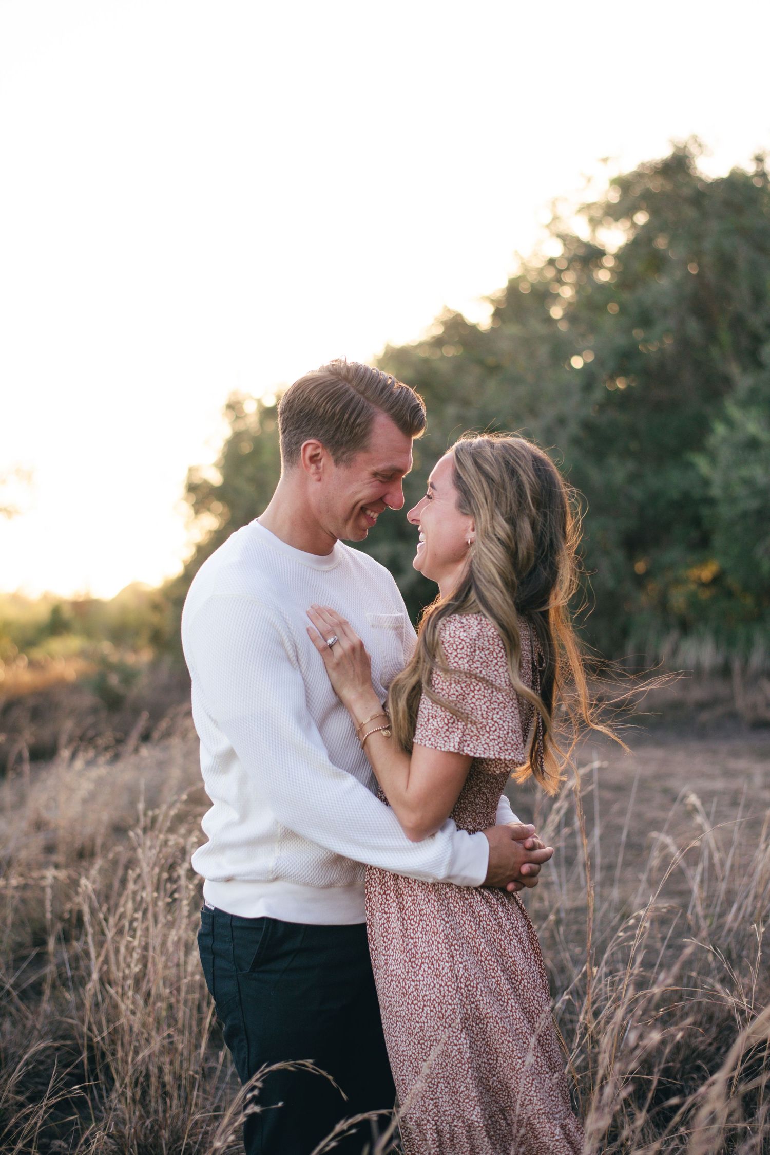 A couple shares a romantic moment in a field of tall grass during golden hour sunset.