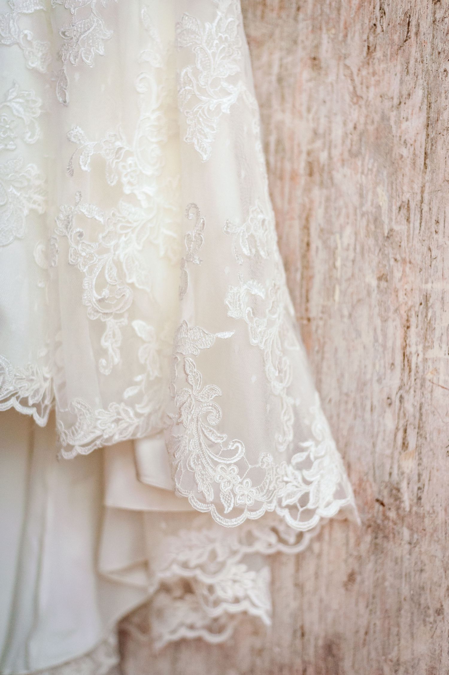 Delicate lace detail of ivory wedding dress hem against rustic wooden background.