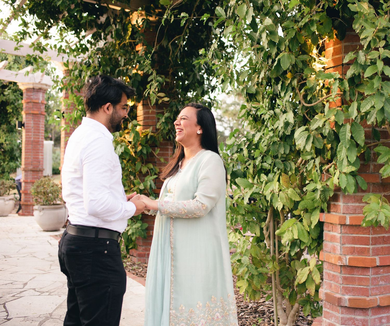 Outdoor engagement photoshoot in a garden setting with brick columns and leafy vines.