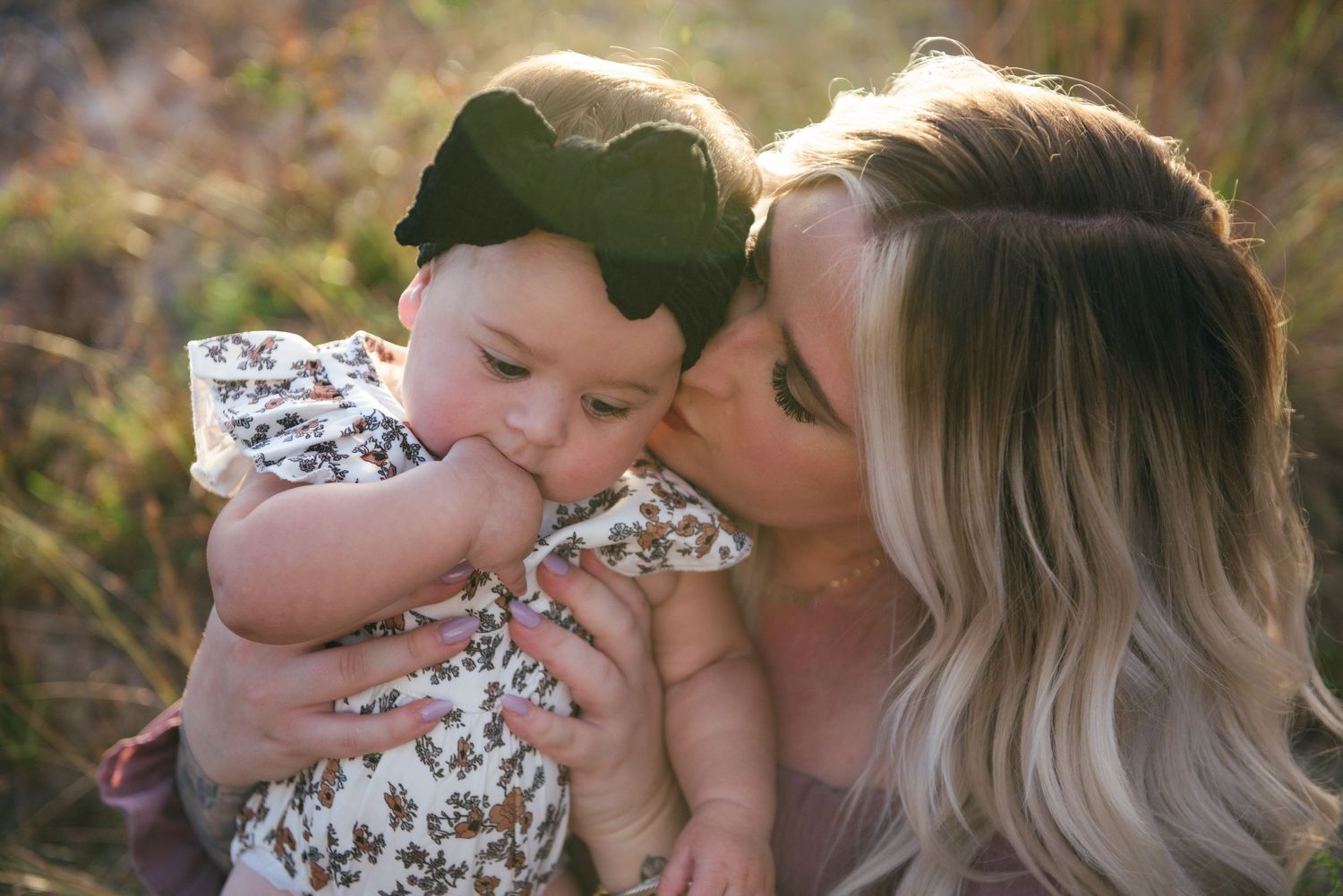Tender moment between caregiver and baby outdoors in warm sunlight.