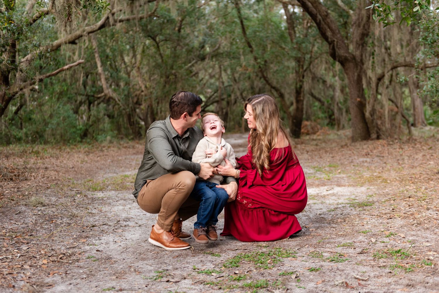 People and their dog enjoy a casual outdoor photo session in a wooded setting wearing red and neutral colors.