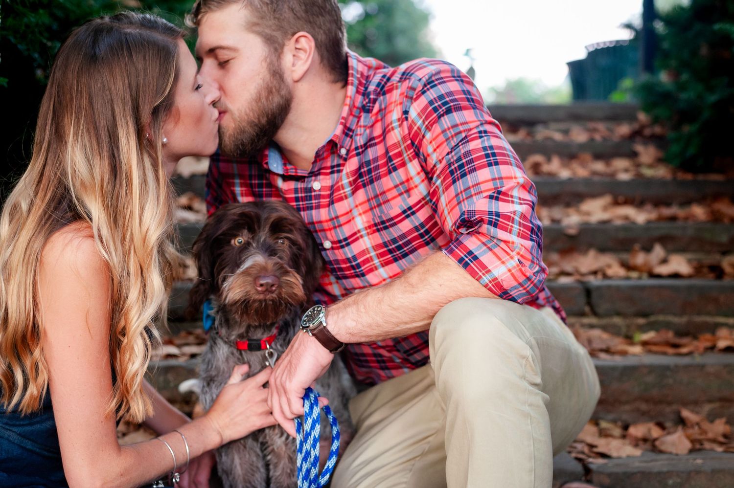 Sweet moment with a couple cuddling by autumn steps while their small brown dog joins them.