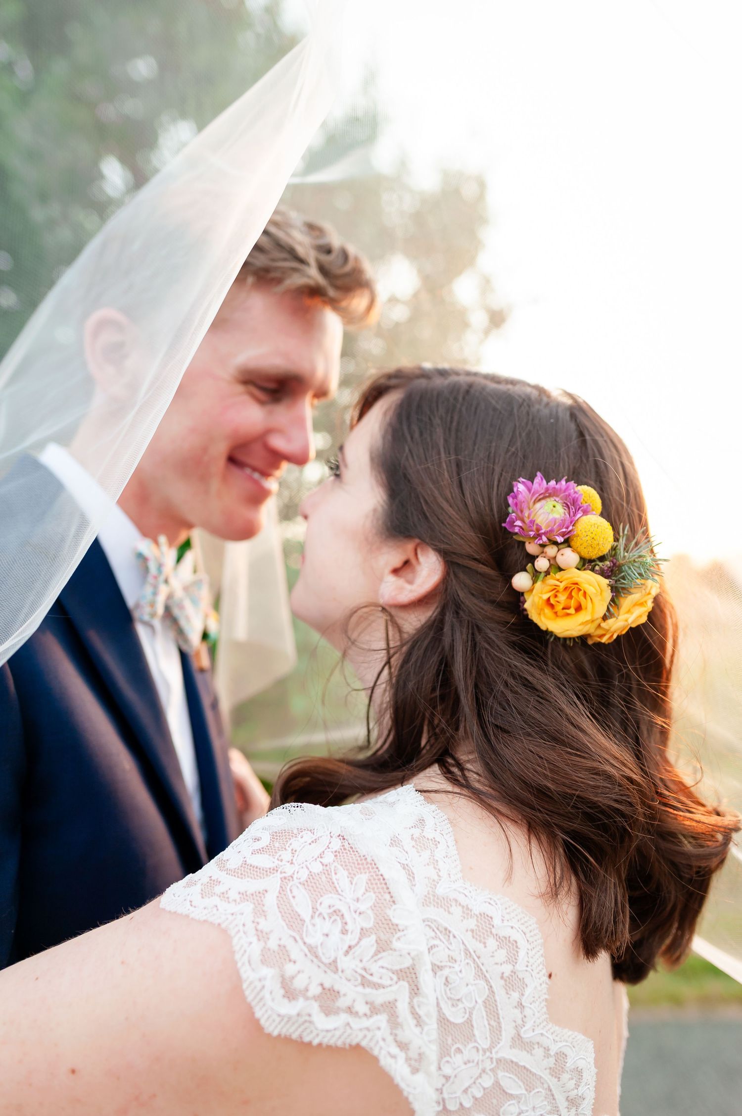 Romantic wedding moment captured with bride wearing floral hairpiece under flowing veil at sunset.