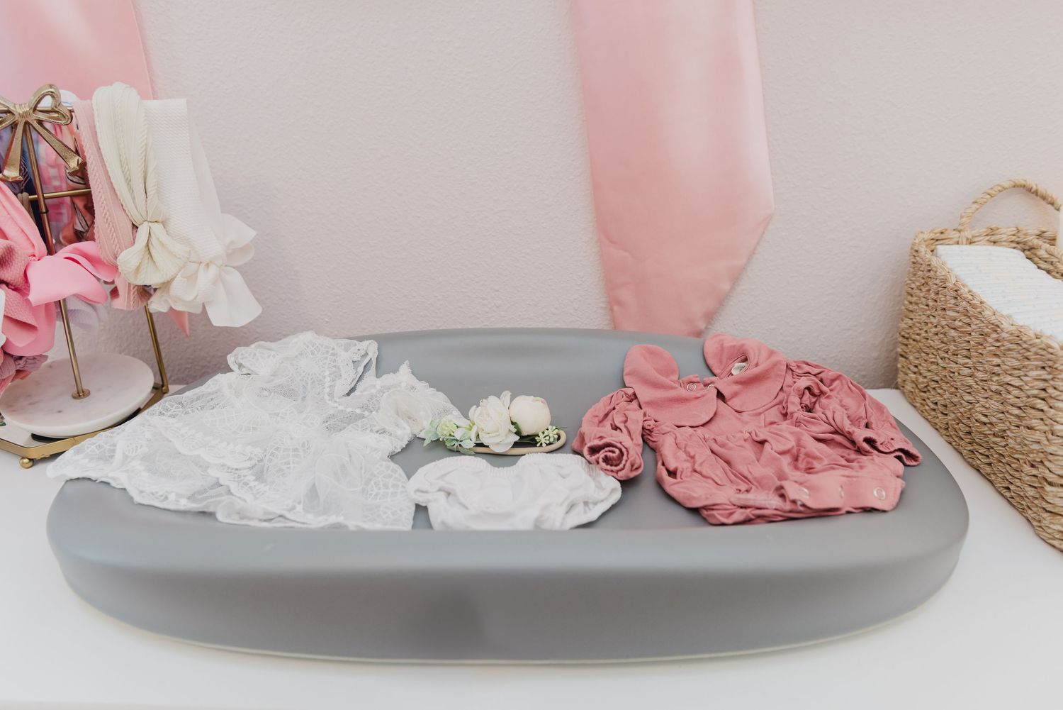 Pink and white baby clothes and accessories arranged neatly in a nursery setting.