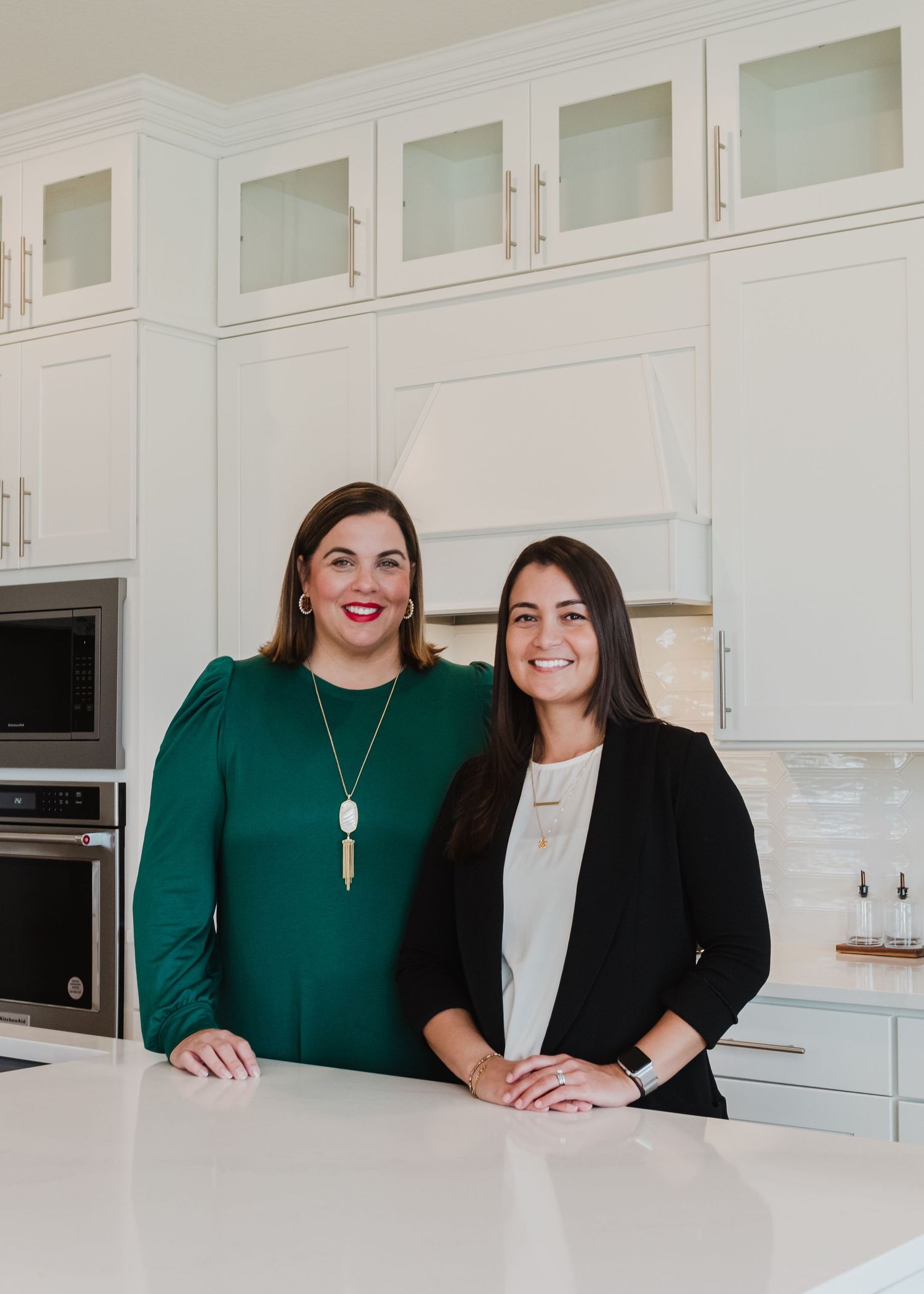 Two professionals standing in modern white kitchen with glass cabinet doors.