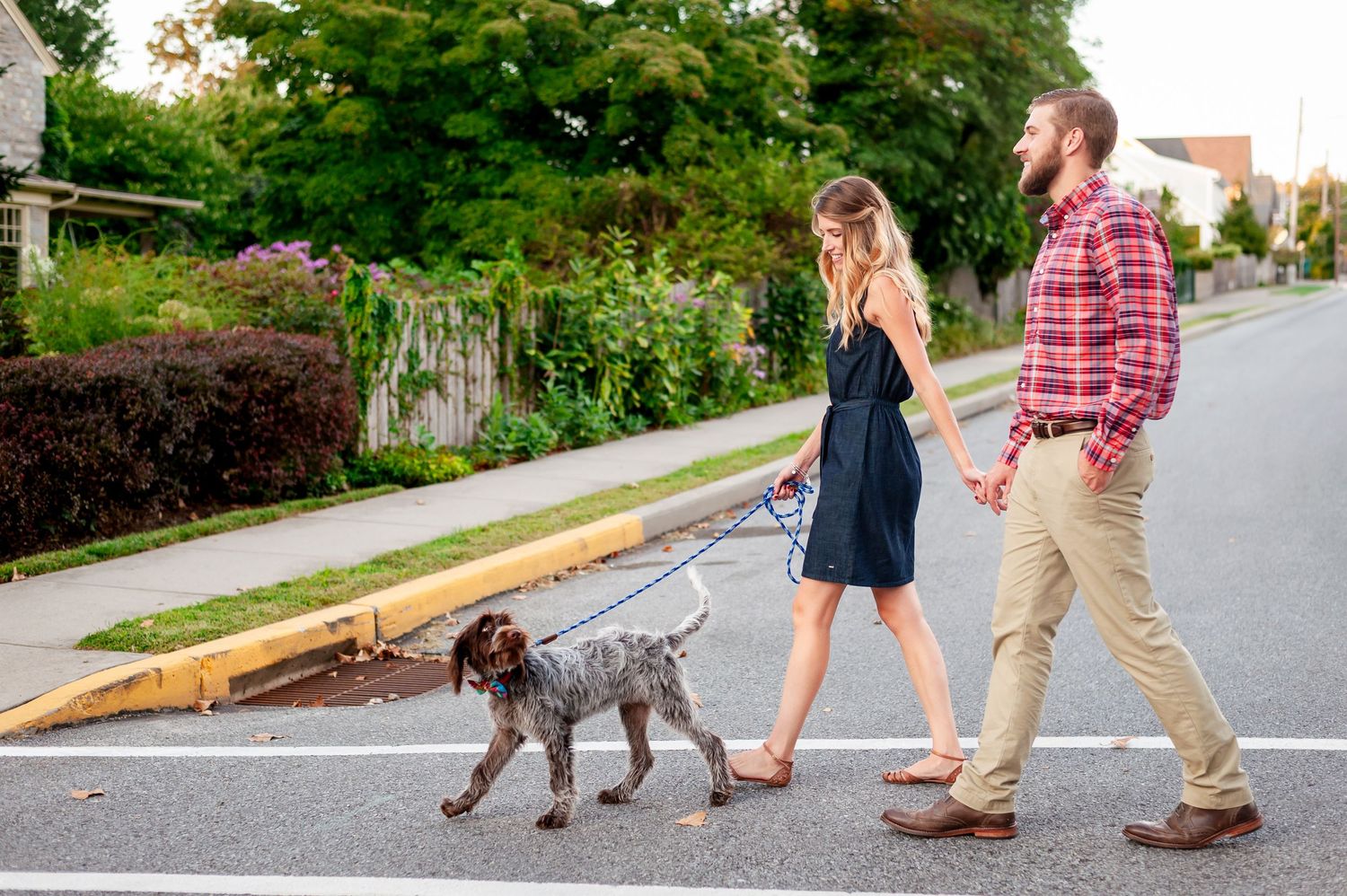 Couple walking their dog together on a residential street during a casual outdoor stroll.