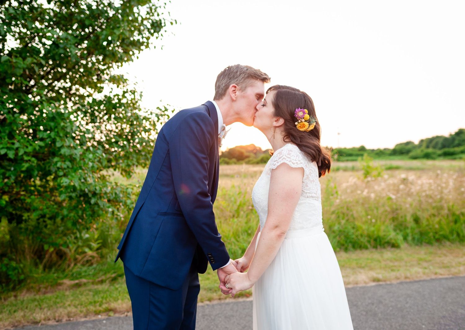 Happy couple embraces on rural path during sunset wedding photoshoot.