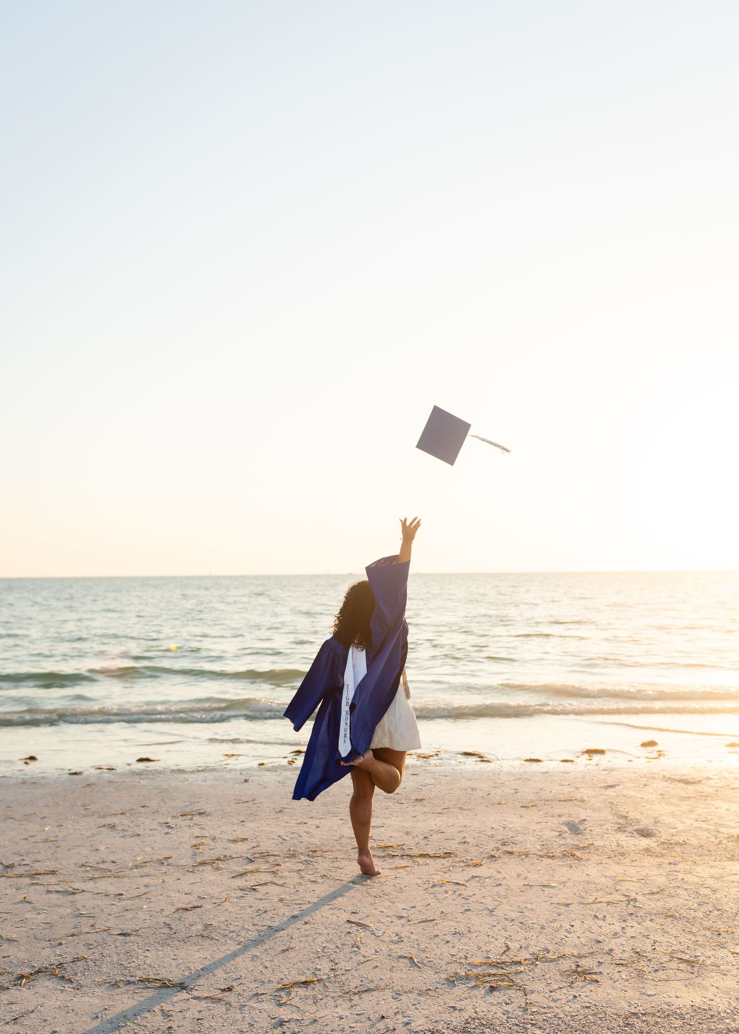 Silhouette of graduate tossing cap in the air on beach at sunset.