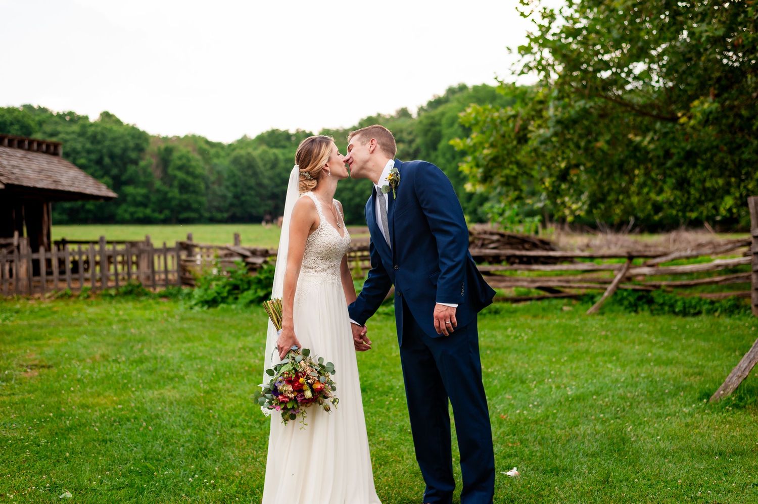 Romantic wedding portrait with rustic barn and stone wall backdrop.