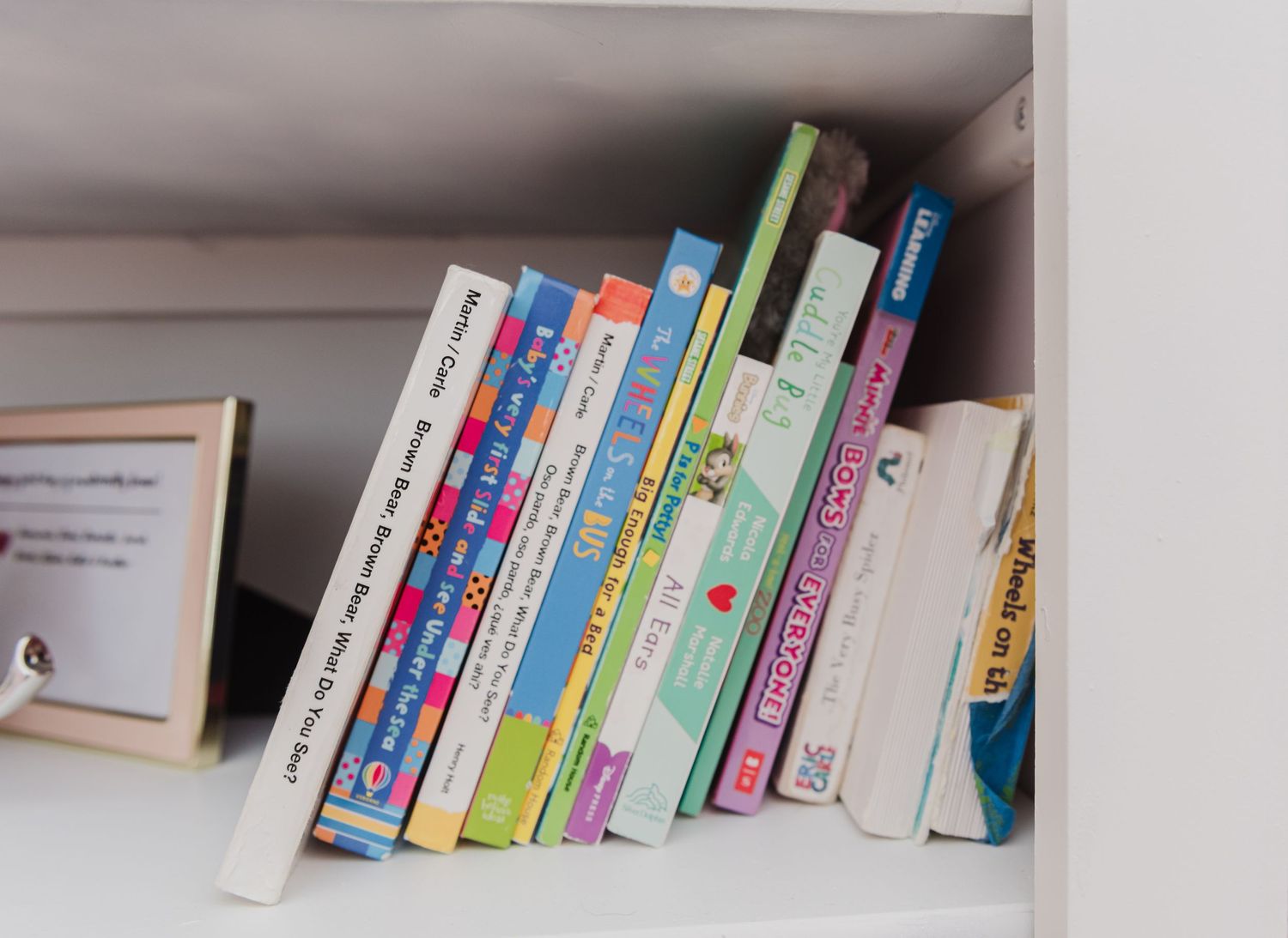 Collection of children's books neatly arranged on white bookshelf shelves.