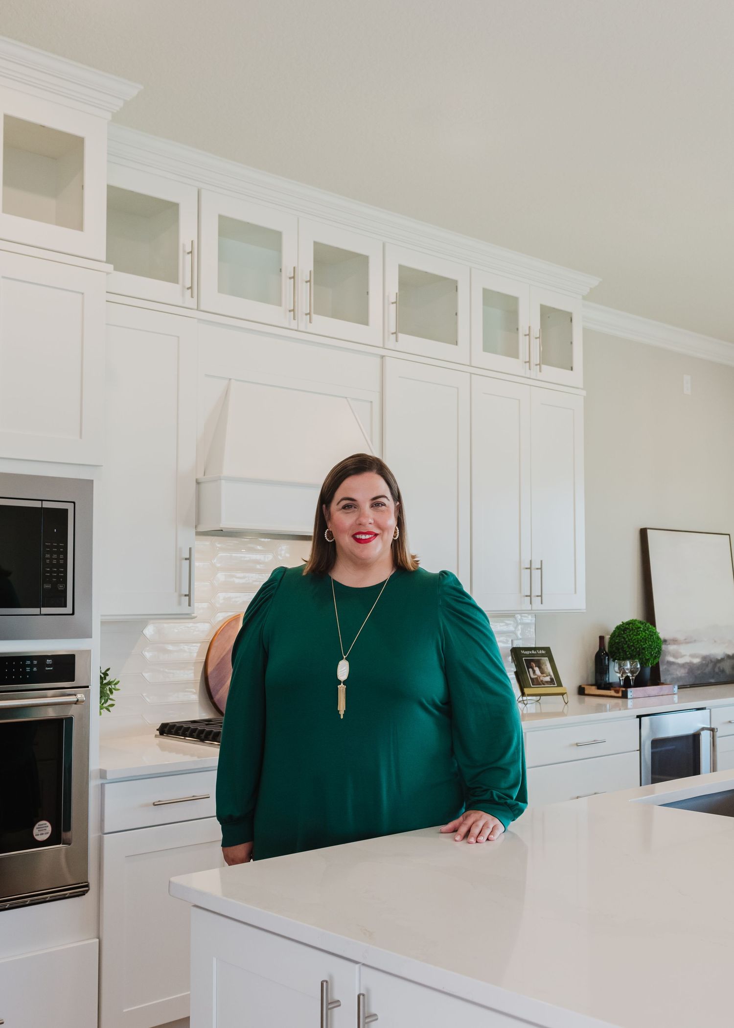 Professional in emerald green blouse posing at modern white kitchen counter.