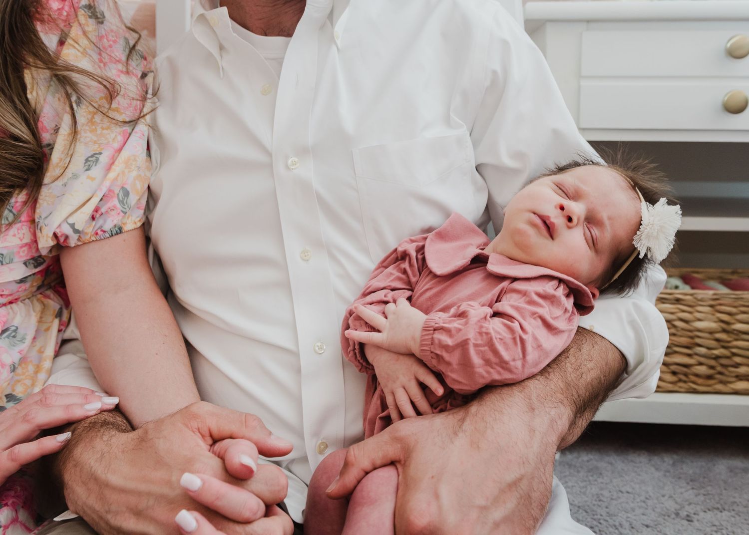 Close-up of sleeping newborn baby in pink outfit being held by parent in white shirt.