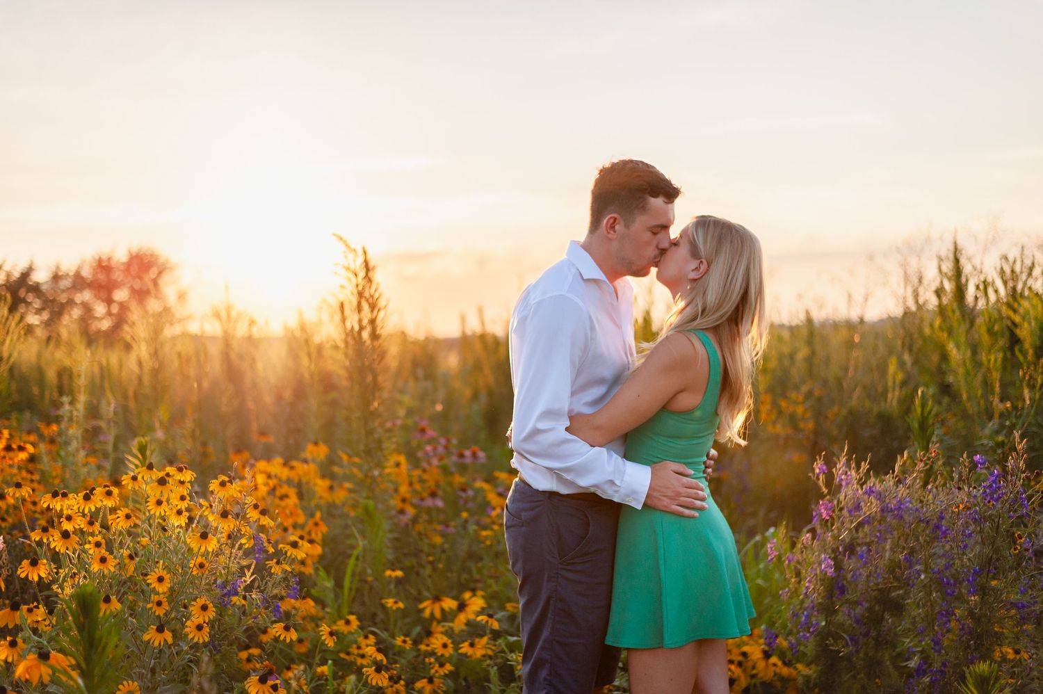 Romantic couple embrace among colorful wildflowers during golden sunset.