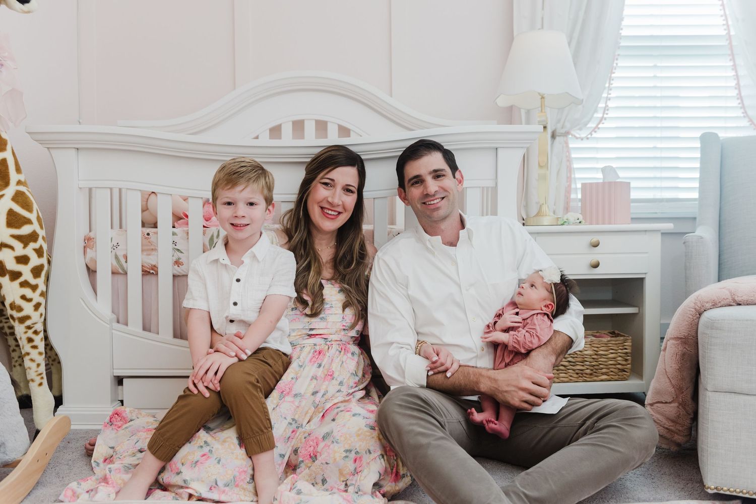 Family photo in nursery with white crib and giraffe plush toy.