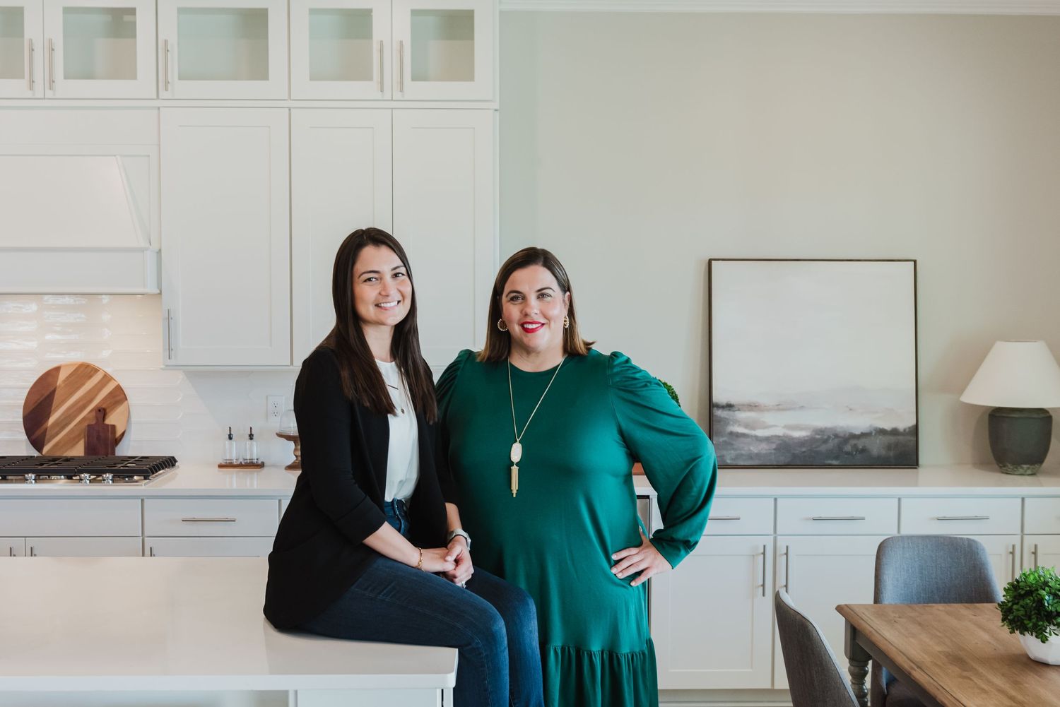 Two businesswomen standing together in a modern white kitchen interior.
