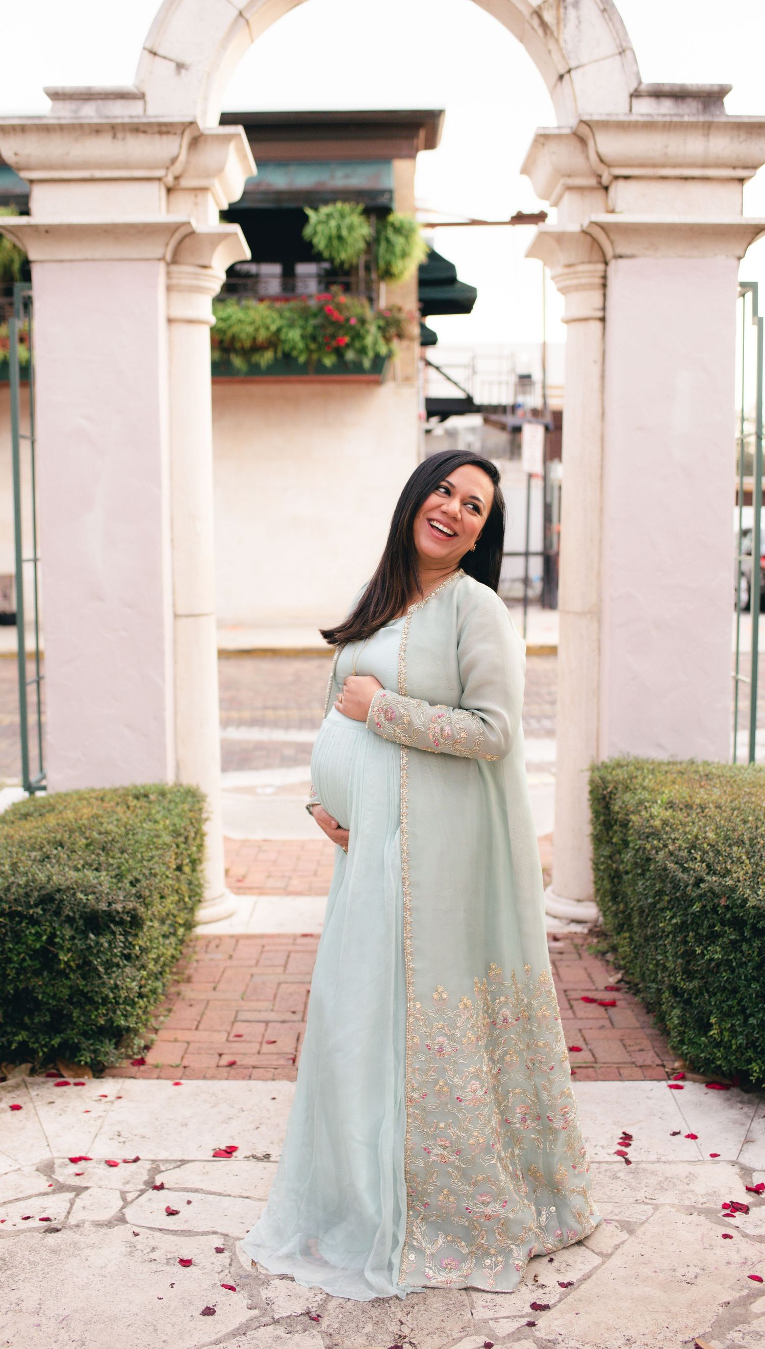 Elegant mint green traditional gown with embroidered details photographed under white stone archways with landscaped hedges.