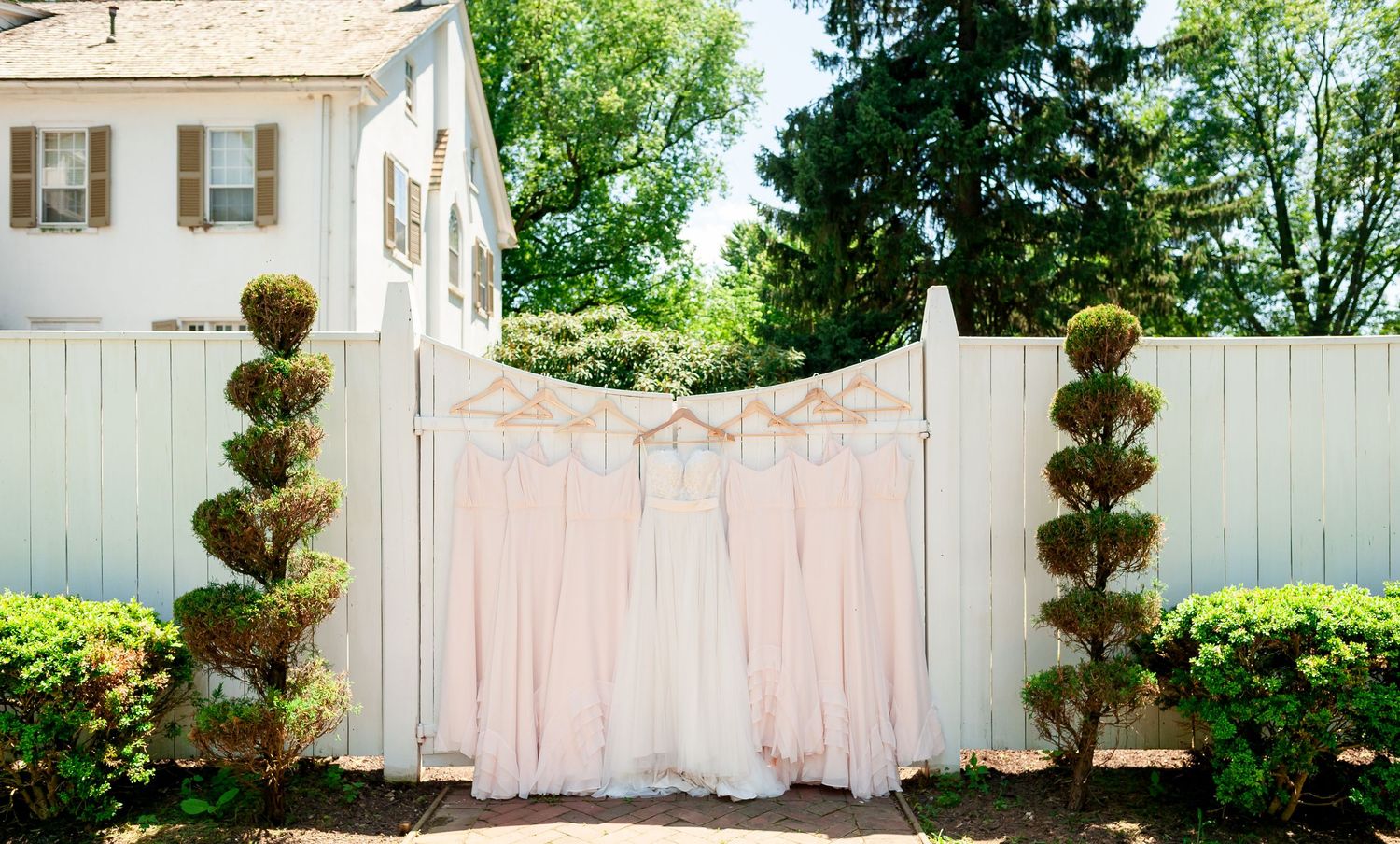 White garden gate decorated with spiral topiaries and sheer pink fabric panels.