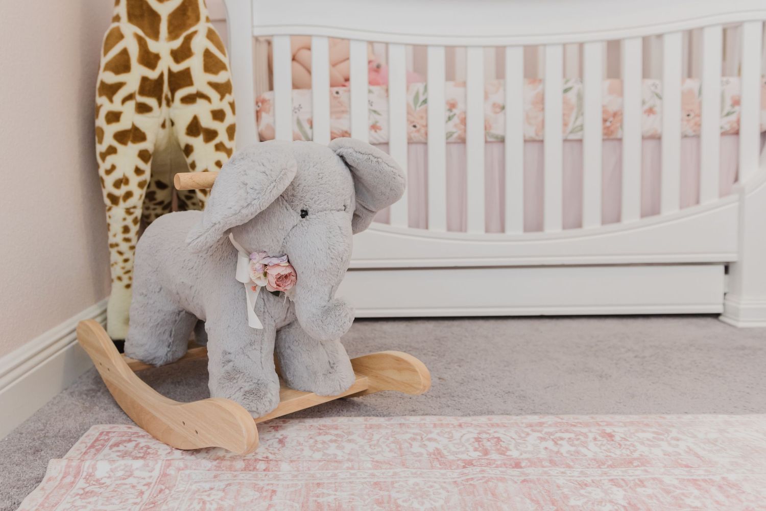 White crib with giraffe print decor and a plush rocking elephant in a nursery.