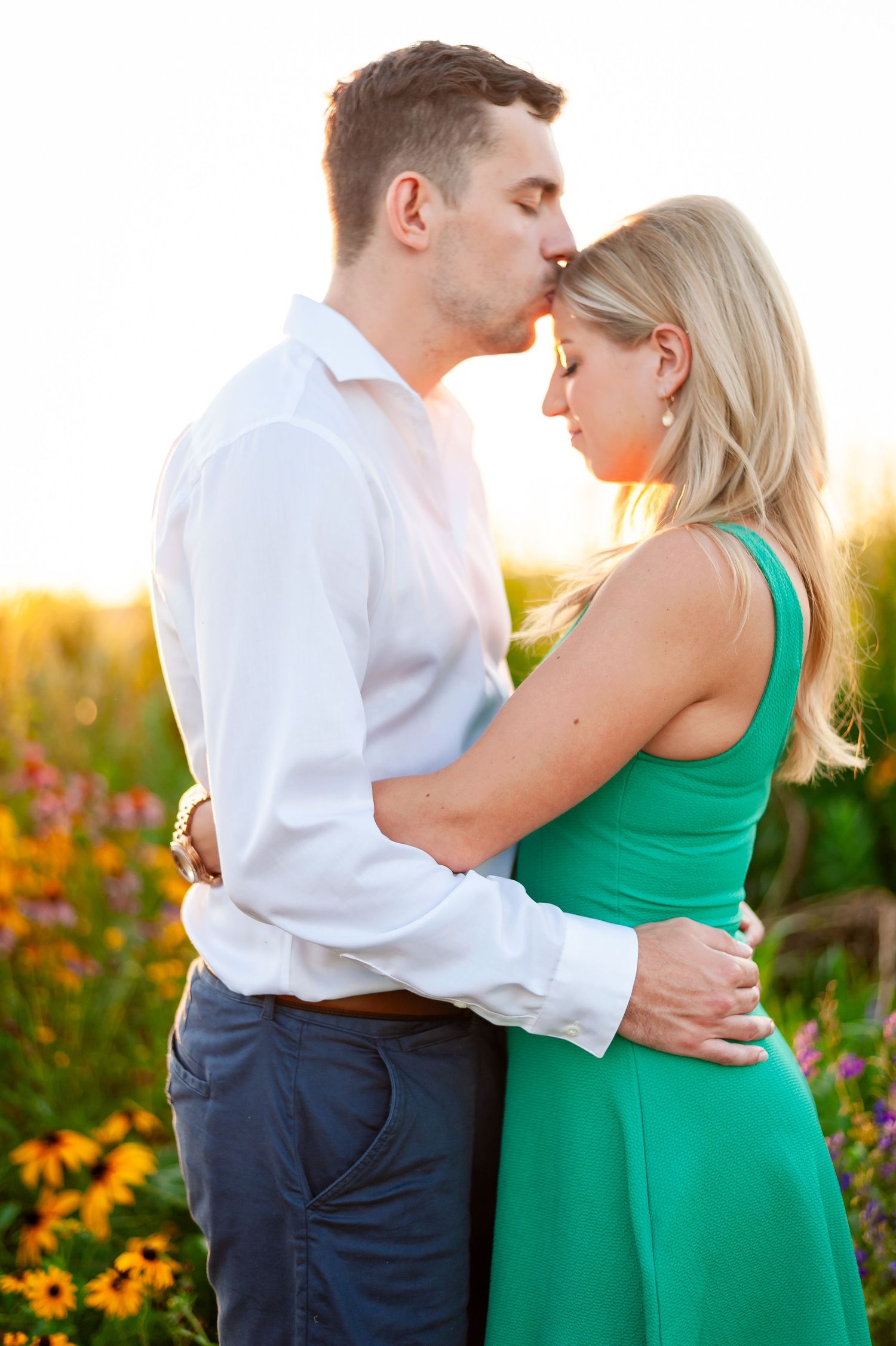 Intimate moment between couple in white shirt and green dress with sunset backdrop.