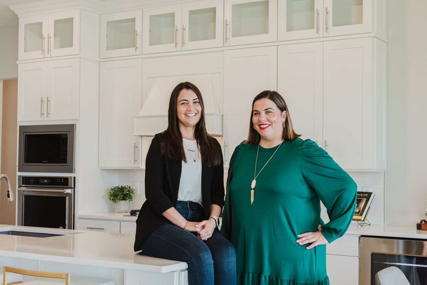 Business professionals in black and green outfits posing in bright modern kitchen.