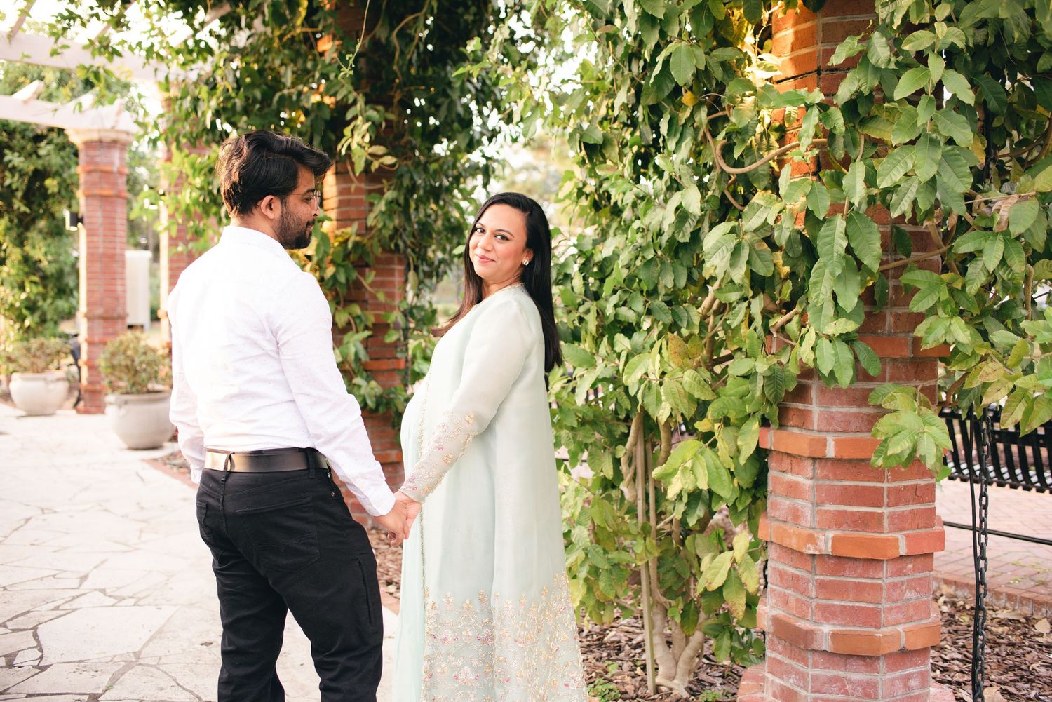 Two people stand in front of a brick and vine covered wall while having an outdoor photoshoot.