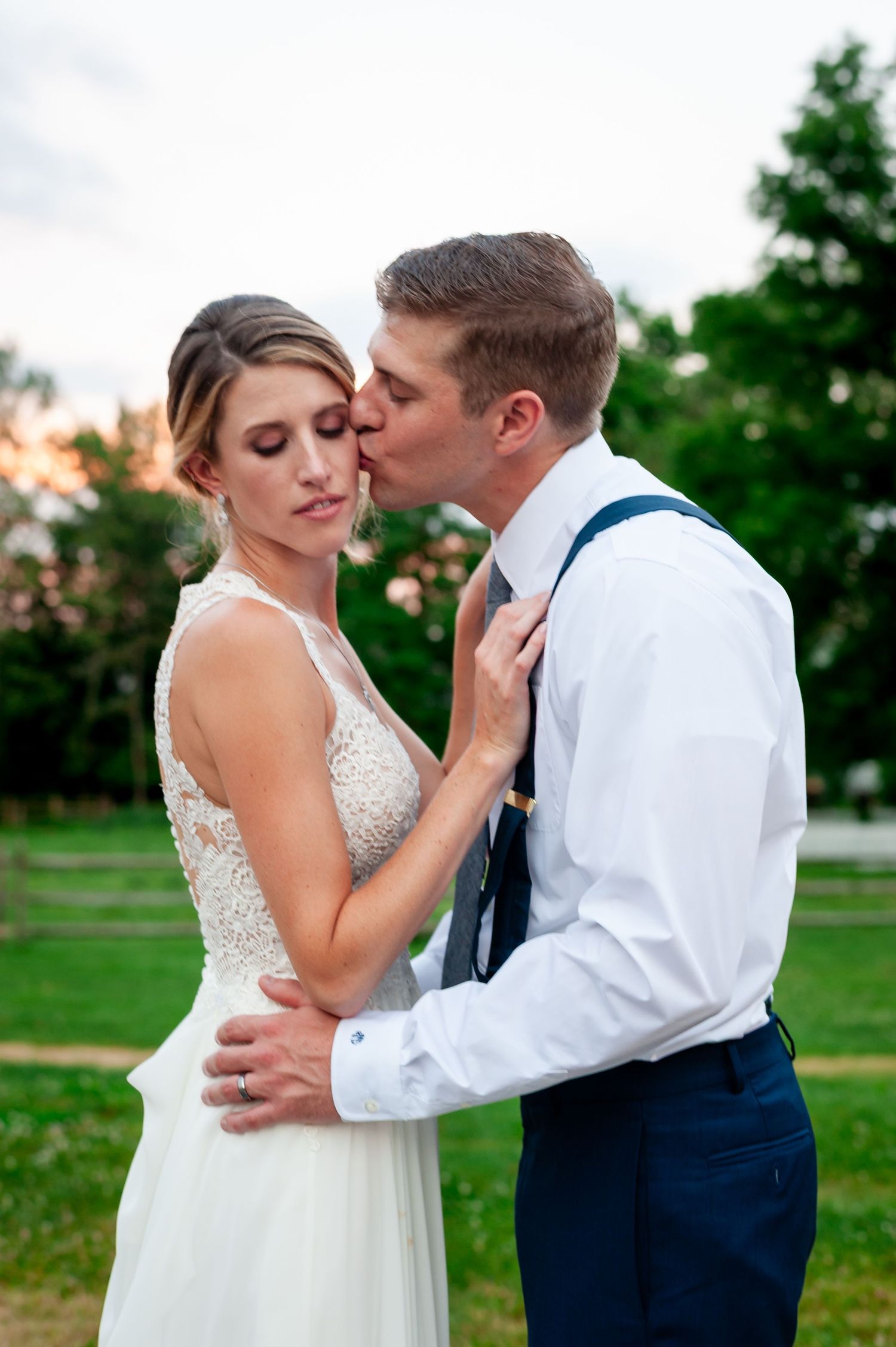 Romantic sunset embrace between newlyweds with the groom in suspenders and rolled sleeves.
