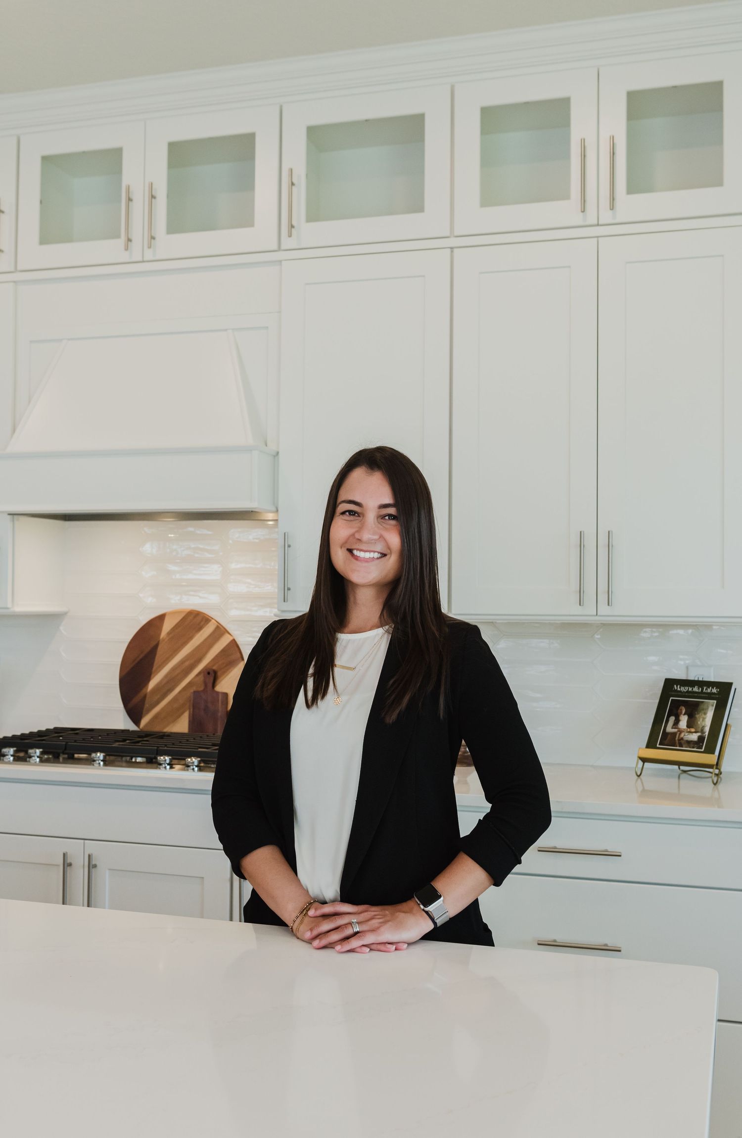 Professional smiling while seated at white kitchen counter with modern cabinets.