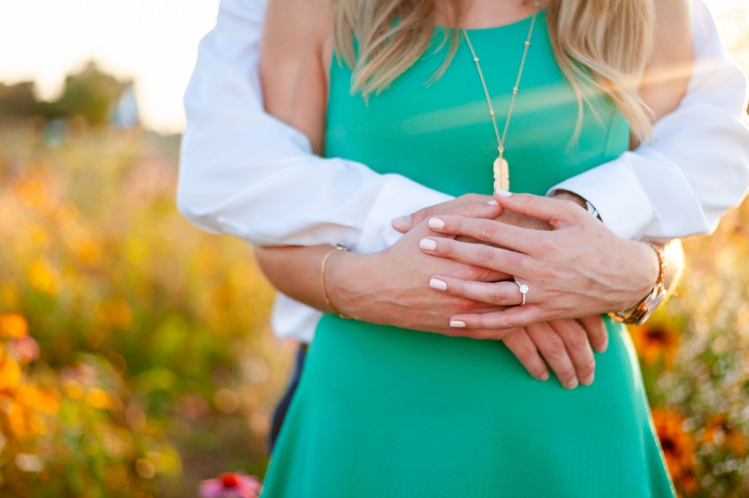 Close up of hands embracing in front of vibrant wildflowers during golden hour sunset.
