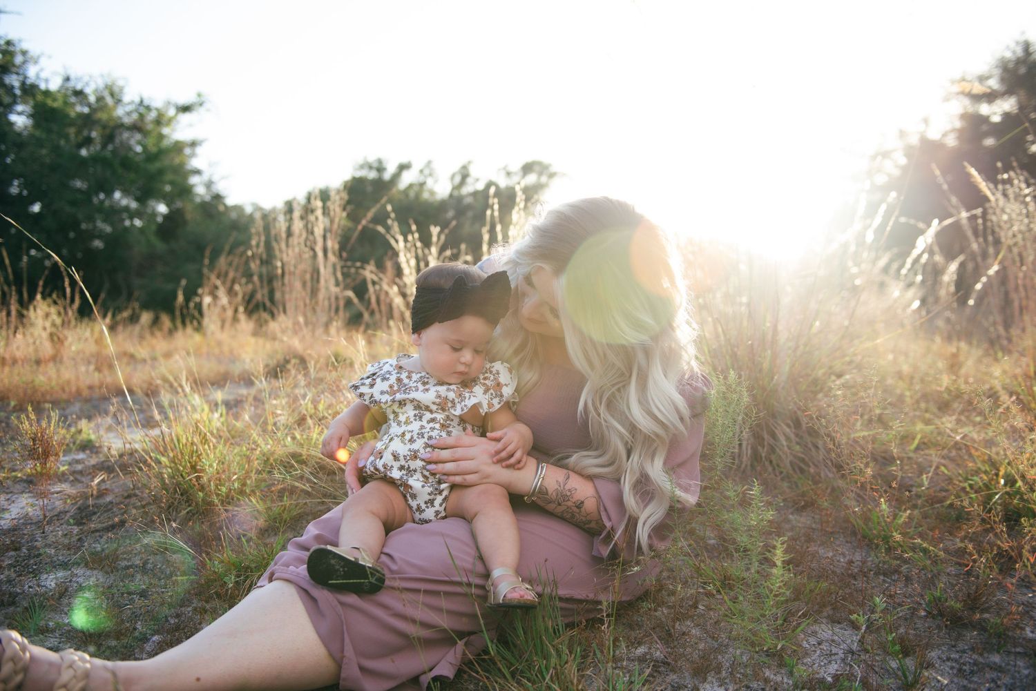 Sunlit outdoor portrait of caregiver and baby in natural setting.