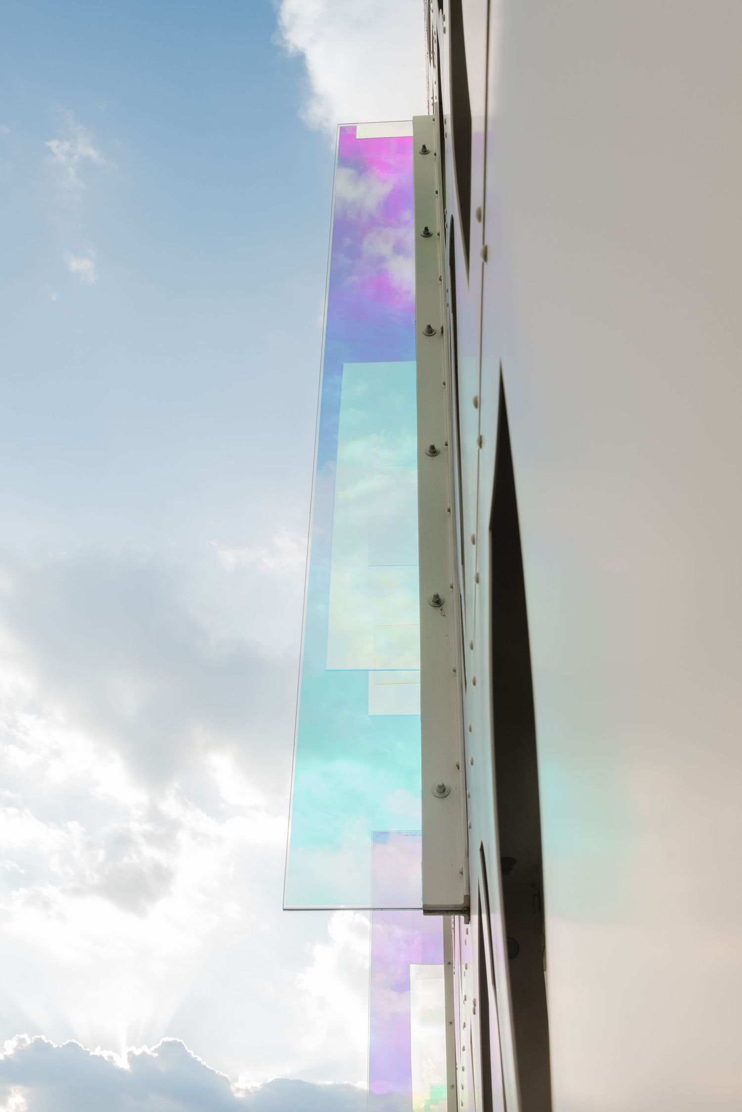Iridescent architectural glass panels reflecting sunlight against a blue sky.
