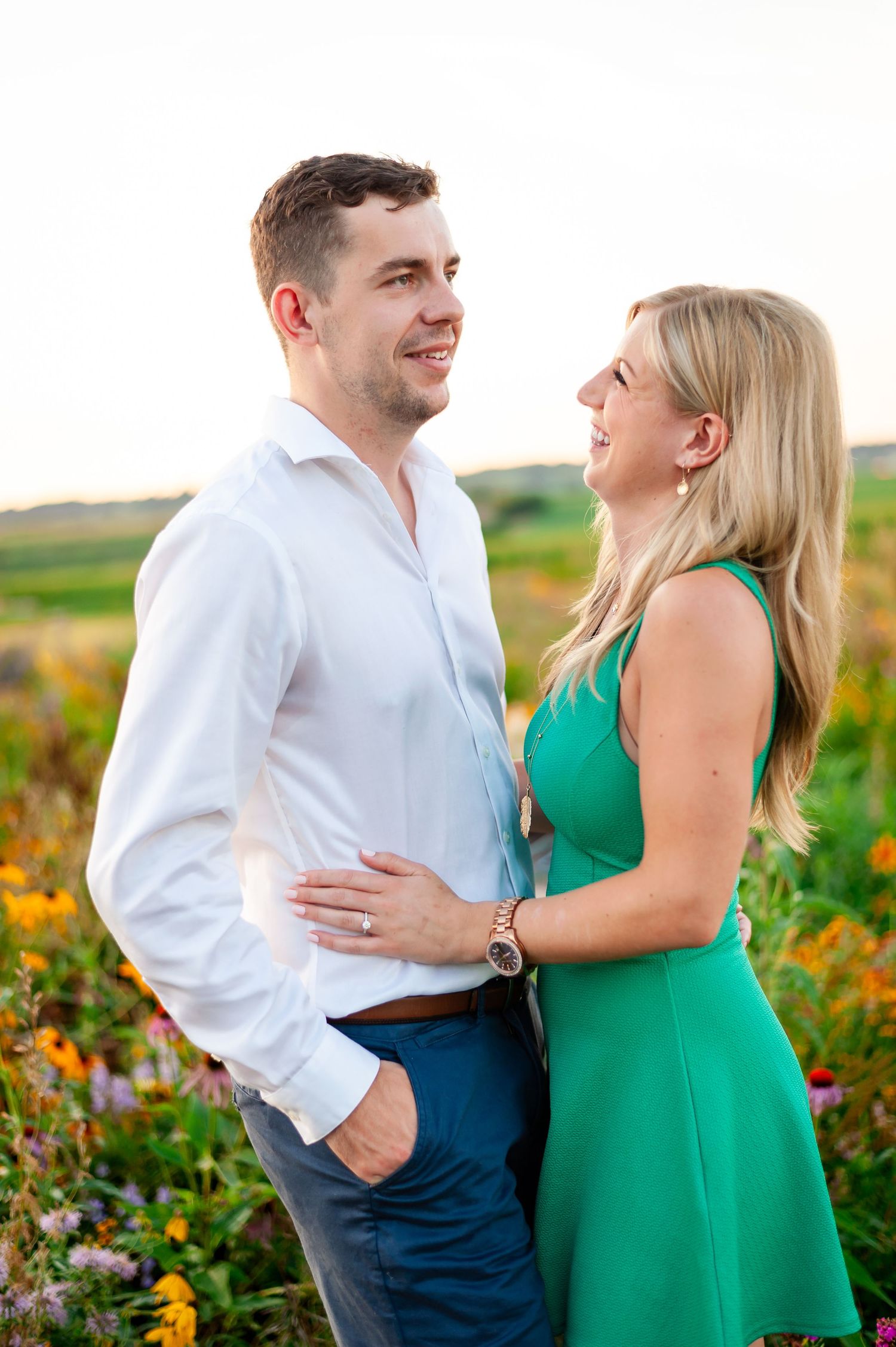 Romantic couple embraces in a vibrant wildflower meadow at sunset wearing green and white outfits.