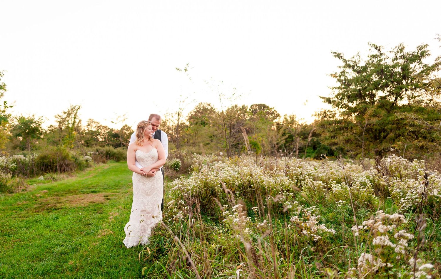 Golden sunset illuminates outdoor wedding portraits in natural meadow setting.