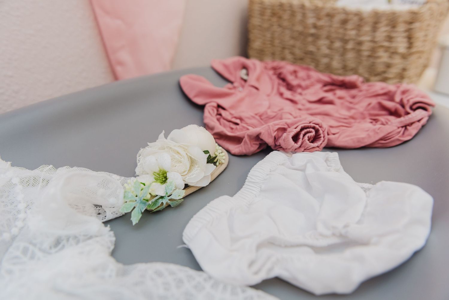 Delicate white and pink baby clothes displayed on a gray surface with floral accents.