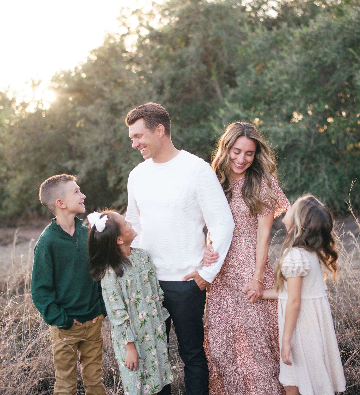 A family walking together outdoors at sunset in a field with trees in the background.