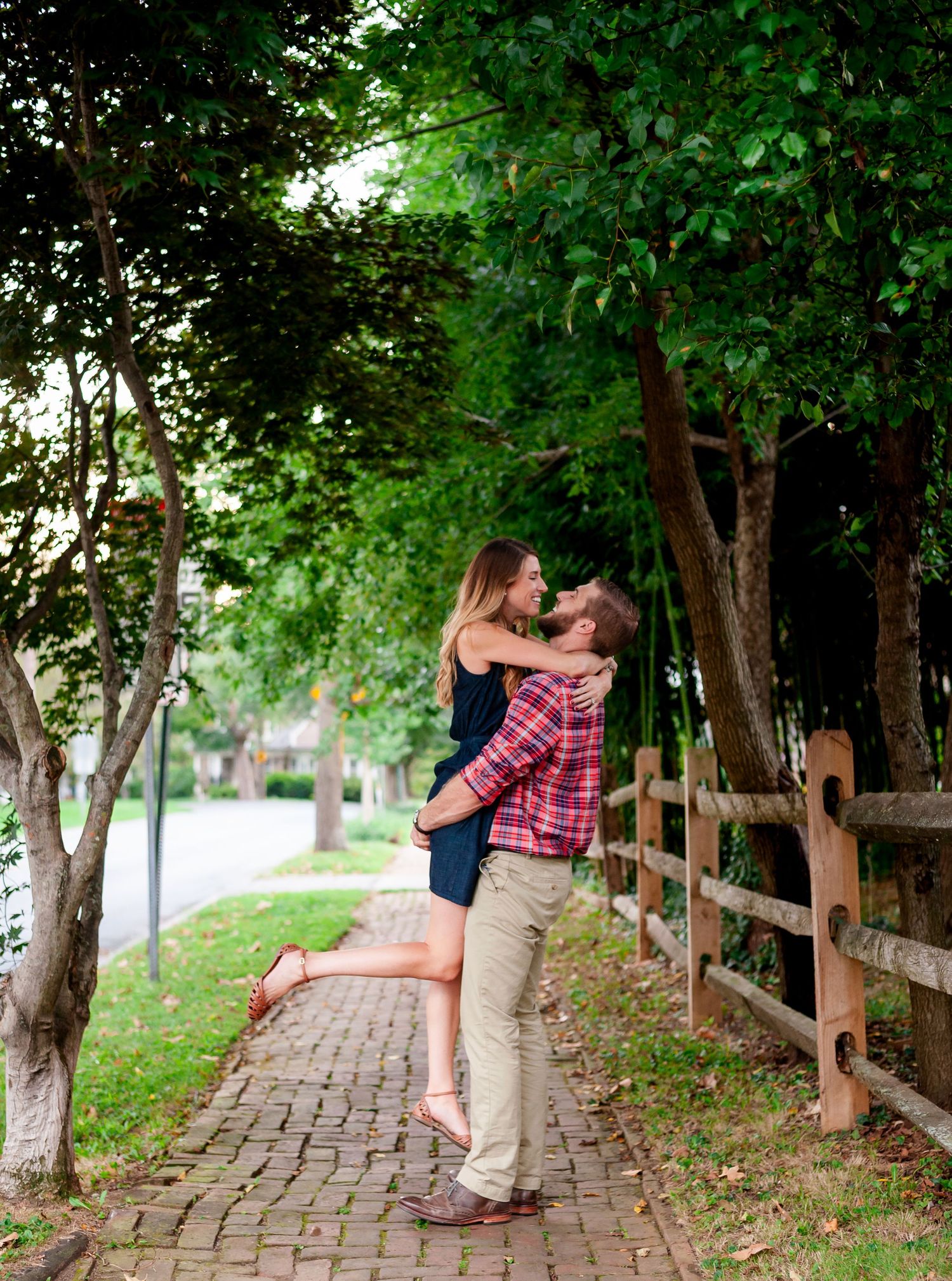 Couple sharing a romantic moment together on a charming brick path lined with trees and a wooden fence.