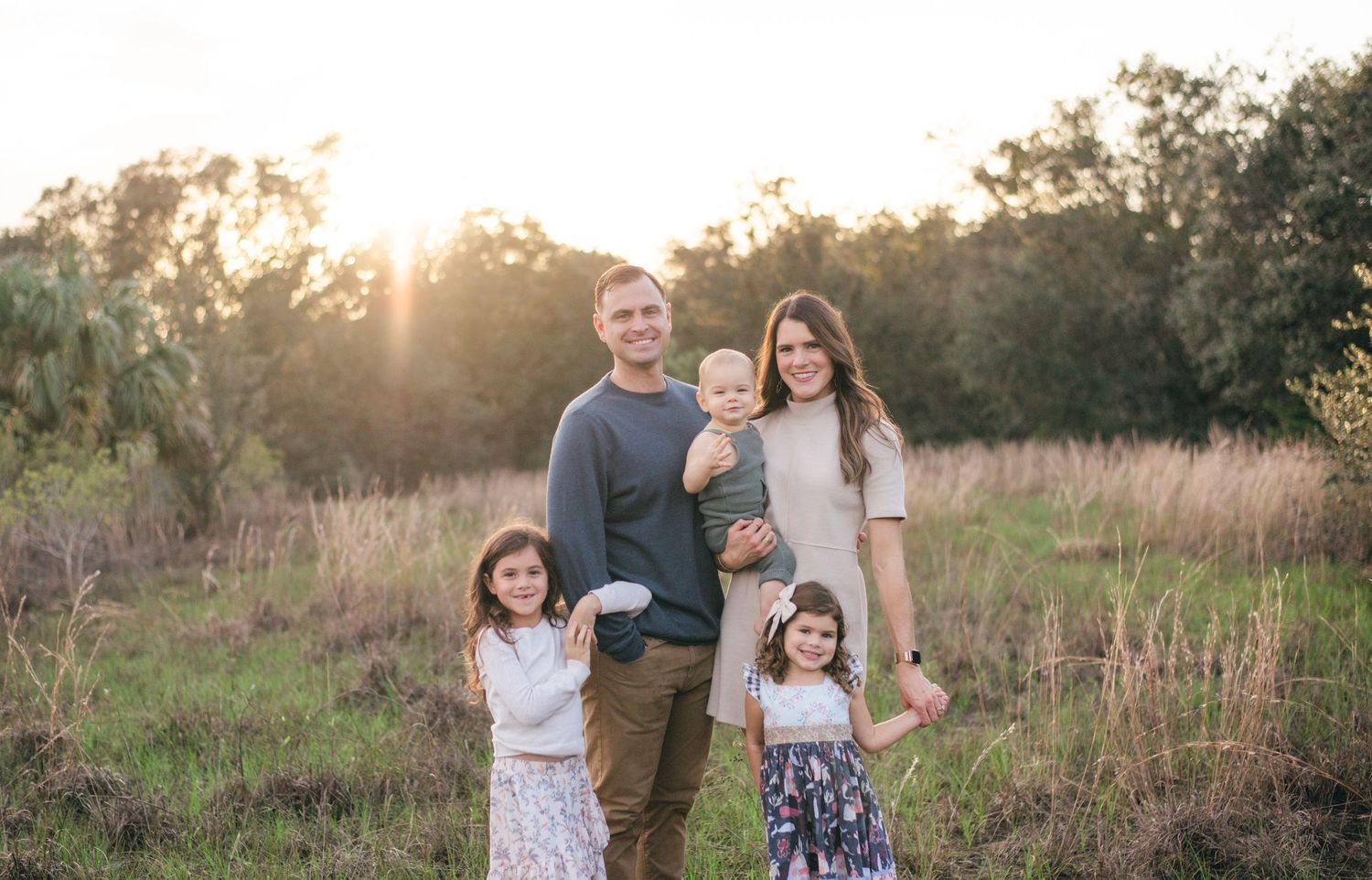A family of five stands together in a sunlit field of tall grass during golden hour.