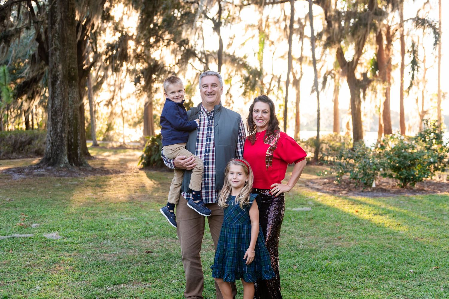 Family poses together in outdoor wooded setting during golden sunset for autumn portrait session.