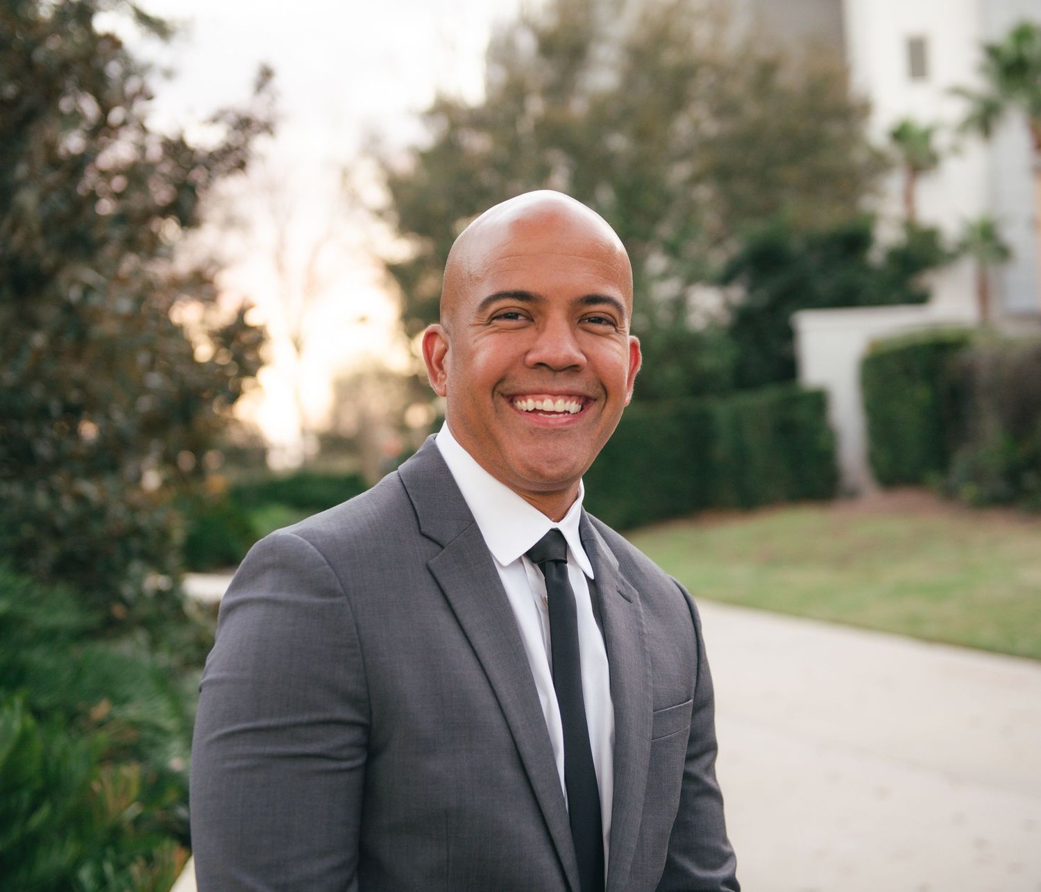 Professional headshots against a natural outdoor backdrop featuring grey suit and black tie.